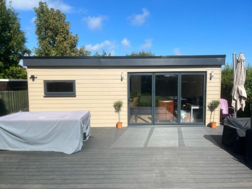 796e3af2-aa3b-4e59-acc6-87bedb7df4ba-optimized Flat-roof garden room extension with large glass doors and timber-effect cladding.
