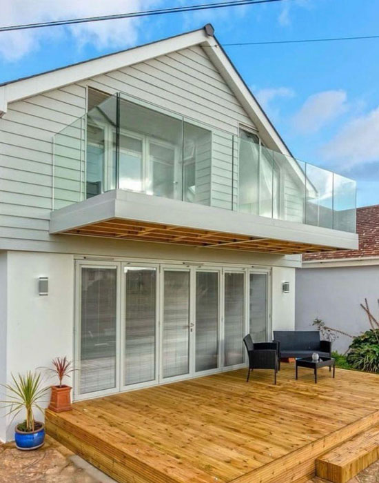 img-loft-conversion-550-700 Modern grey and white cladded house with glass balcony and timber decking.