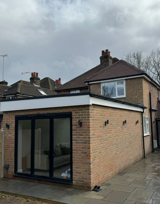img-new-builds-3 Completed single-storey brick extension with black bifold doors and flat roof.