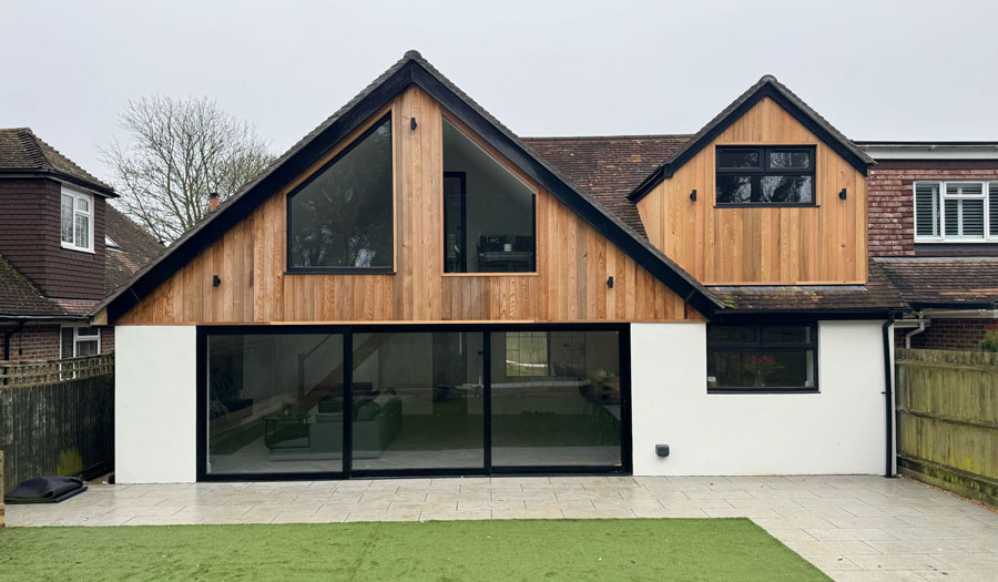 Contemporary new build home with pitched roof, timber cladding, and large glass sliding doors.