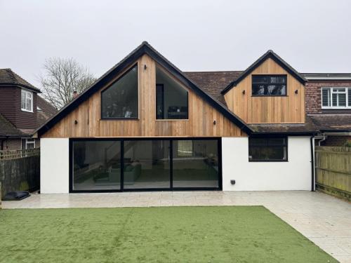 Rear view of finished dormer loft conversion and extension in Aldsworth, showcasing timber cladding and large bi-fold doors.