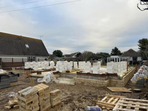 Stacked building materials and foundation outlines for new build properties on active Worthing development site.