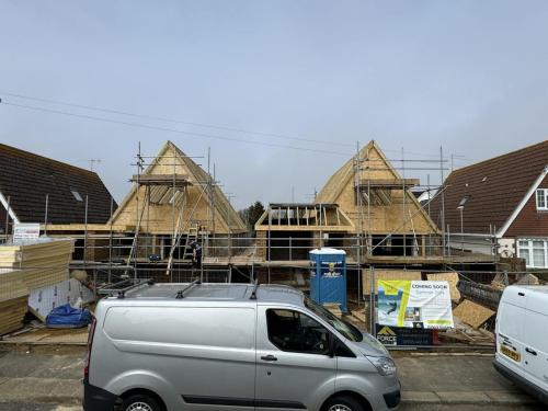 Timber roof frames going up on detached new build homes in Worthing, with scaffolding and site signage in place.